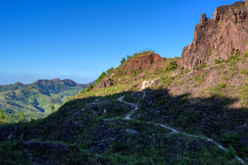 Naklejka premium Dirt road in shadow of rock mountain with blue sky
