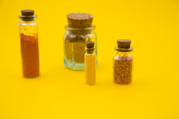 Glass bottles with dry spices and fresh herbs on a wooden cutting board with yellow background, top view, close up