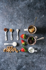 Chocolate and vanilla caramel mug cakes from microwave with fresh strawberries and ingredients in spoons above over blue texture background. Top view, space. Food knolling