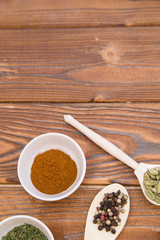 Plastic spoons and cups with dry spices and fresh herbs on a wooden rough boards background, top view, close up