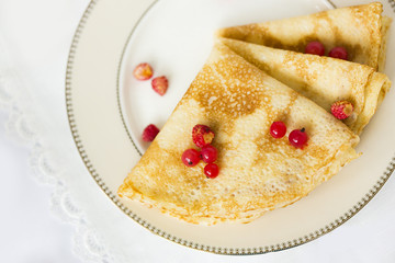 Тонкие блины, свернутые треугольниками со свежими ягодами красной смородины и земляники на белой фарфоровой тарелке