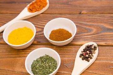 Plastic spoons and cups with dry spices and fresh herbs on a wooden rough boards background, top view, close up