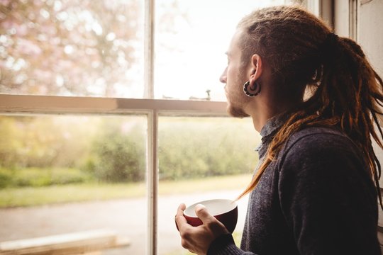 Hipster holding coffee cup while looking through window