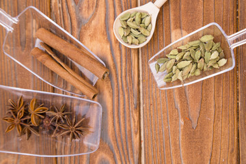 Glass spoons with dry spices and fresh herbs on a wooden rough boards background, top view, close up