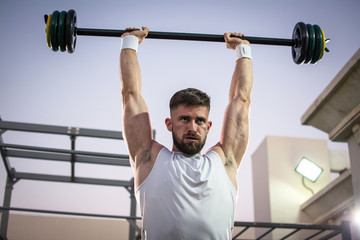 Fototapeta na wymiar Muscular young man lifting barbells in public gym.