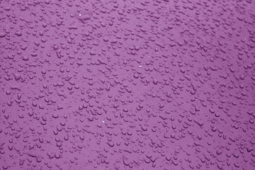 Water drops on blue color metal surface with blur effect in purple color.