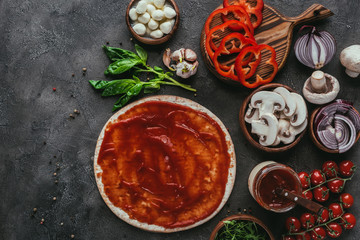 top view of raw pizza dough with sauce and vegetables on concrete table