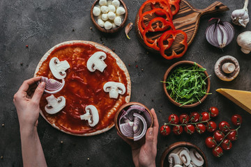 cropped shot of woman spreading onion slices onto pizza on concrete table