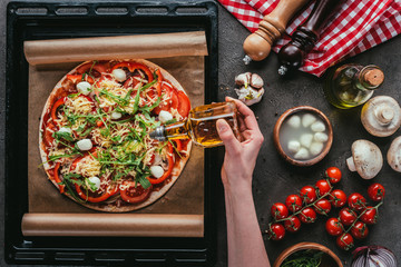 cropped shot of woman pouring oil onto delicious pizza on concrete table