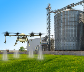 Agriculture drone flying on the green rice fields with Agricultural Silos in the background.