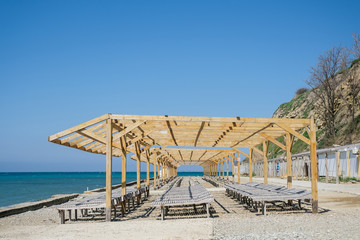 Wooden sun loungers on a pebbled public beach by the sea.