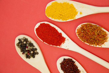 Plastic spoons with dry spices and fresh herbs on a rose background, top view, close up