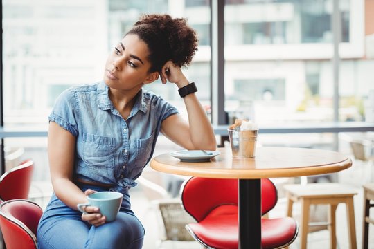 Smart thoughtful woman holding coffee cup in restaurant