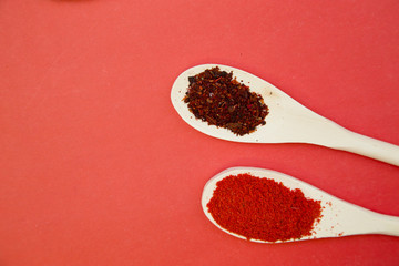 Plastic spoons with dry spices and fresh herbs on a rose background, top view, close up