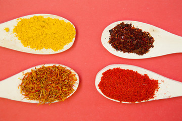 Plastic spoons with dry spices and fresh herbs on a rose background, top view, close up