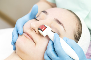 The woman undergoes the procedure of medical micro needle therapy with a modern medical instrument derma roller 