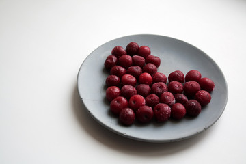 Heart shaped valentine composition of frozen cherries covered with melting ice isolated on grey concrete plate