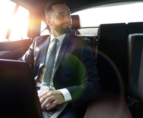 man with laptop sitting in the back seat in the car