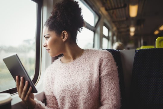 Woman looking through window while holding digital tablet 