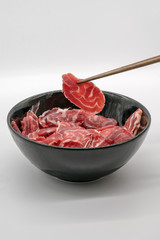 Chopstick holding fresh sliced beef hind shank from black ceramic bowl