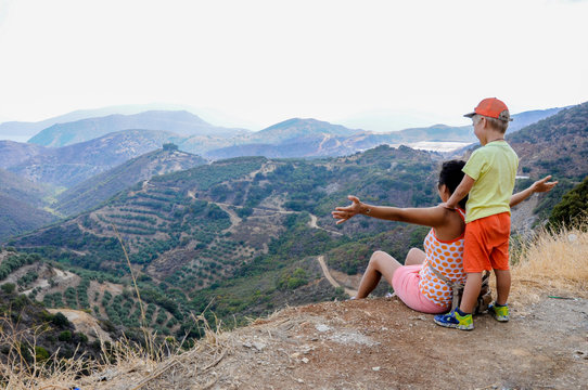 Child boy with his mother looking at beautiful summer mountains landscape and olive groves. Family travel Europe,Crete, Greece, august. Top view on olive groves and Mountains in Background.