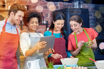 happy friends with tablet pc cooking in kitchen