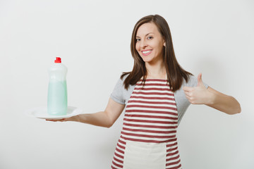Young housewife in striped apron isolated on white background. Housekeeper woman holds bottle with cleaner liquid for washing dishes, white empty round plate. Bottle with copy space for advertisement.