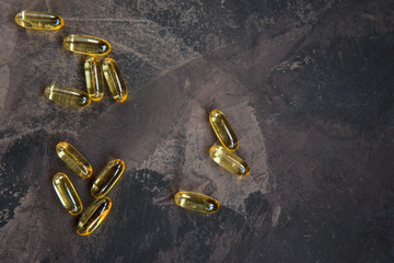 Yellow vitamin capsules on a dark background, soft gelatin capsule with oily drug