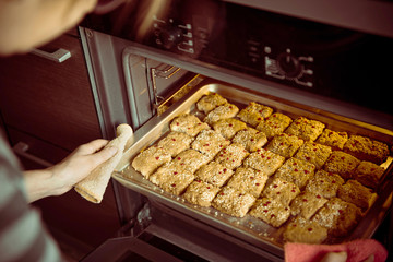 Female hands take a baking tray with a shortbread cookie from the oven. Retro photo toning.