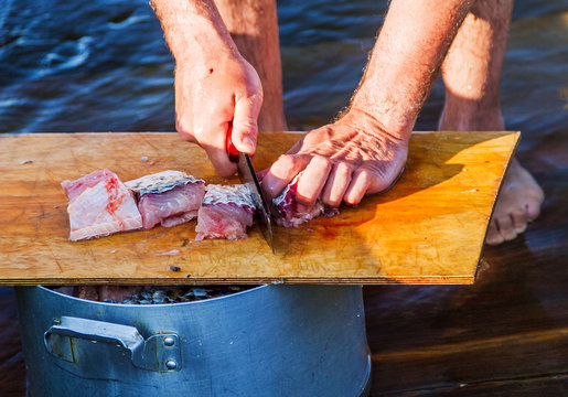 A barefoot fisherman knifes a carp fish with a knife on a board on the deck