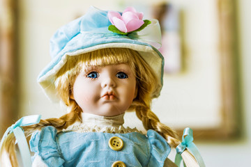 Close-up of beautiful porcelain doll with blond hair and blue eyes, sky blue vintage dress and leather shoes. Little princess games.