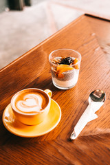 Chia pudding with yogurt, granola, mango, cranberries on wooden coffee table. Hipster coffee shop. Minimalistic food photography concept
