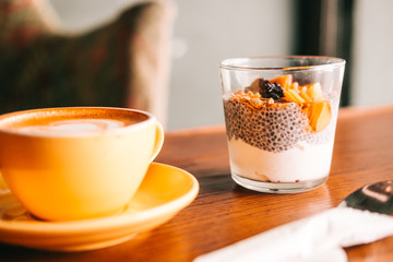 Chia pudding with yogurt, granola, mango, cranberries on wooden coffee table. Hipster coffee shop. Minimalistic food photography concept