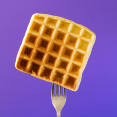 Belgian waffle with honey decorated sweet cherry pinned on a fork on violet background