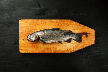 Fresh fish on a wooden vintage cutting board on a dark background, top view