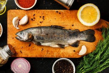 Fresh fish with herbs and spices on vintage cutting board on dark background, top view