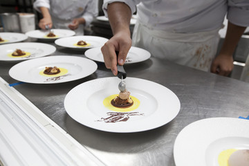 The chef prepares desserts with ice-cream for dinner party in restaurant kitchen.