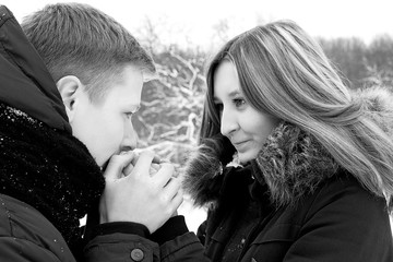 The guy gently warms his hands with the young girl, lovingly looks into her eyes, she sincerely smiles.  Young couple, first love.