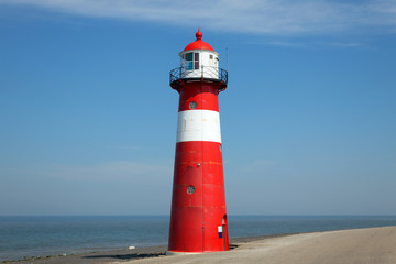 Red lighthouse on a dike seawall by the blue sea