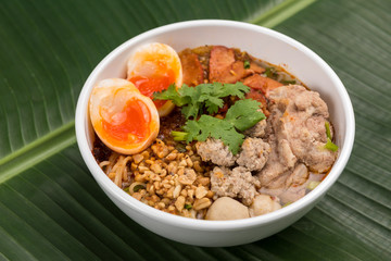 Spicy noodle soup with pork and egg in bowl on banana leaf