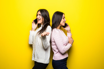 Portrait of a happy girls talking on mobile phones isolated over yellow background