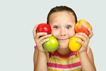 Fototapeta na wymiar Cheerful little girl with apples and lemon poses positively in studio