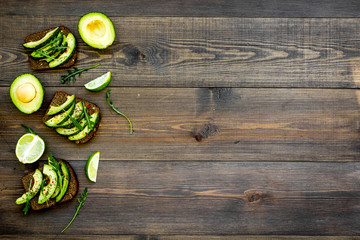 Have a bite with healthy snacks. Avocado toast on dark wooden background top view copy space