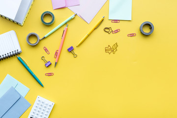 Scattered stationery on student's desk. Yellow background top view copy space