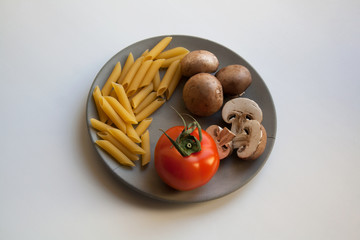 Heap of penne rigate pasta, brown champignon mushrooms and ripe tomato isolated on grey concrete plate