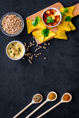 Hummus ready to eat. Bowl with dish among pieces of crispbread and spices on black background top view copy space