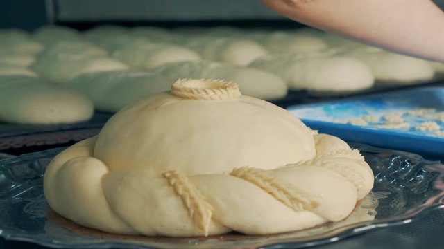 Baker decorating a round loaf with pieces of dough turning the plate around, close up