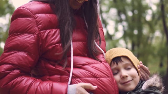 Cute son embracing and listening pregnant belly of mother