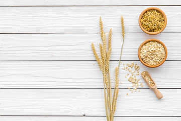 Food which rich with slow carbohydrates. Oatmeal and oat in bowls near sprigs of wheat on white wooden background top view copy space