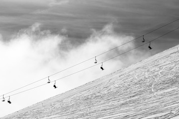 Snow off-piste ski slope and silhouette of chair-lift in fog